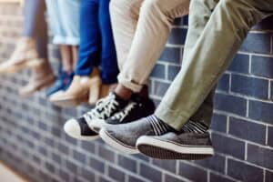 Brick wall, student feet and friends outdoor on university campus together with sneakers. relax, urban youth and foot at college with people legs ready for education, study and shoes while sitting
